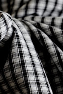 Charcoal and ecru seersucker fabric with a small gingham check, draped in flowing folds revealing the characteristic puckered seersucker texture.