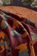 Tissu Seraphine bordeaux plié, avec un bol en céramique sombre contenant des boutons gris-vert.