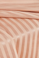 Tissu satin rayé rose poudré drapé sur une chaise en cannage, effet lustré et fluide.