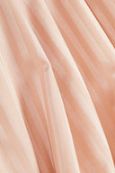 Gros plan sur les plis du tissu satin rayé rose poudré, laissant apparaître le lustre des rayures ton sur ton.