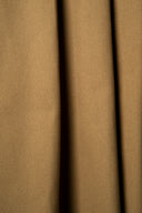 Tissu gabardine camel suspendu en plis verticaux fluides, lisière effilochée visible sur le côté.
