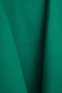 Tissu gabardine vert émeraude drapé en plis fluides sur des volumes architecturaux blancs, jeu d'ombre et de lumière.