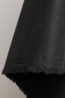 Gros plan sur le tissu gabardine léger noir, avec la lisière effilochée visible sur le bord replié.
