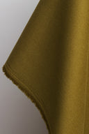 Gros plan sur le tissu gabardine léger vert olive doré, avec la lisière effilochée visible sur le bord replié.