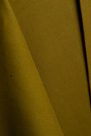 Tissu gabardine légère vert olive doré drapé en plis fluides sur l'angle d'un socle blanc.