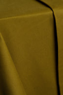 Gros plan sur le tissu gabardine léger vert olive doré, plié en angle sur un support, mettant en valeur sa texture fine.
