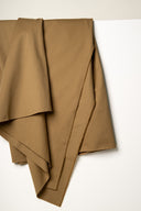 Tissu gabardine légère camel drapé en plis superposés, lisière effilochée visible sur plusieurs épaisseurs.