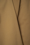 Gros plan sur les plis diagonaux du tissu gabardine légère camel, laissant apparaître la lisière perforée.