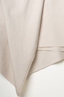 Gros plan sur le pli en pointe du tissu gabardine légère beige argile, texture sergé fine visible.