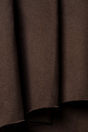 Gros plan sur les plis drapés du tissu gabardine marron chocolat, mettant en valeur sa texture sergé mate.