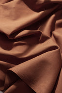 Tissu gabardine caramel drapé en plis fluides sur des volumes architecturaux blancs, jeu d'ombre et de lumière.