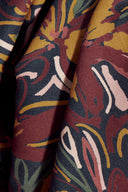 Tissu viscose Hilma bordeaux à imprimé floral graphique moutarde et sauge, drapé sur un banc en bois.