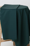 Popelin fabric, forest green, draped over an antique wooden stool, frayed selvedge visible.