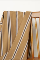 Tissu Weave Line caramel à rayures verticales anthracite et écru, drapé sur le dossier d'une chaise en bois.
