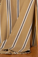 Gros plan sur les plis diagonaux du tissu Weave Line caramel à rayures anthracite et écru, posé sur une chaise en bois.