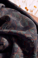 Tissu Vera marine plié, avec des bobines de fil bordeaux et noir en bois, posées sur un bol noir contenant des boutons foncés.