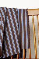 Weave Line chocolate fabric with sky-blue and ecru vertical stripes, draped over the back of a wooden chair, with a frayed selvedge visible.