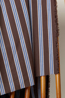 Weave Line chocolate brown fabric with sky-blue stripes, draped over a wooden support with its fringed selvedge visible.